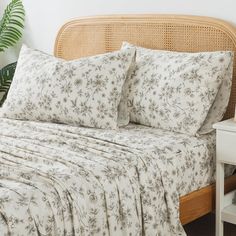 a bed with white sheets and pillows on top of it next to a plant in a pot