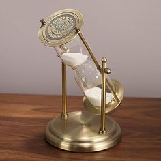 an hourglass with sand in it sitting on top of a wooden table next to a clock