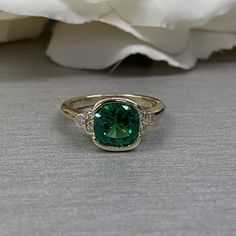 a close up of a ring with a green stone in the middle and diamonds around it