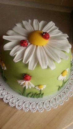 a green cake with white daisies and ladybugs on the top is sitting on a lace doily