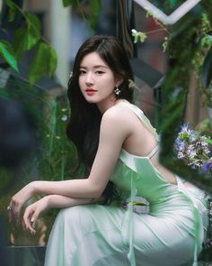 a woman in a green dress sitting on a bench next to some plants and flowers