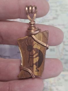 a person is holding a small pendant made out of wood and wire with an animal on it