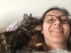 a woman laying on top of a bed next to a brown and black cat with glasses