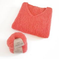 an orange knitted sweater next to a skein of yarn on a white surface