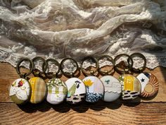 six keychains with different designs on them sitting next to a lace doily