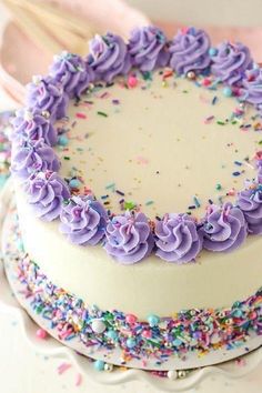 a white cake with purple frosting and sprinkles