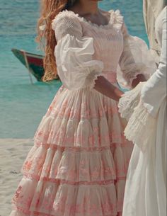 two women in dresses standing on the beach next to each other and looking at something