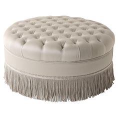 a white round ottoman with fringe trim around the bottom and tassels on top