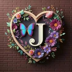 the letter j is surrounded by flowers and butterflies in a heart shaped frame on a brick wall