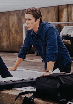 two men are looking at something on the ground with luggage in front of them and one man is holding his hand out