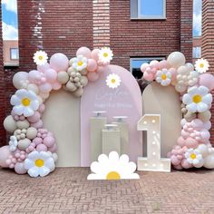 an arch made out of balloons and flowers on the side of a brick building with a sign that says 1