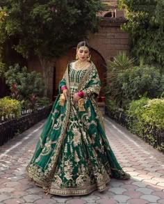 a woman in a green and gold bridal gown standing on a cobblestone walkway