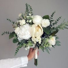 a person holding a bouquet of white flowers in their hand with greenery on the side