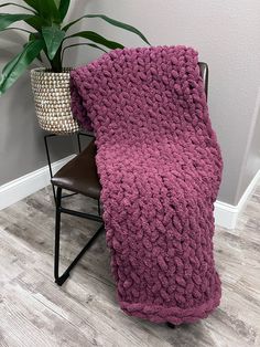 a purple blanket sitting on top of a chair next to a potted plant