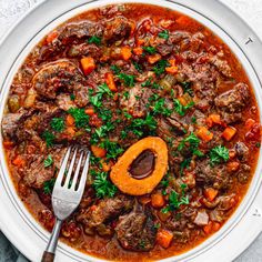 a white plate topped with meat and carrots next to a fork on top of a table