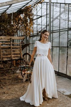 a woman standing in front of a greenhouse wearing a white dress and holding a bouquet