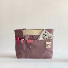 a small bag with some items in it on a white surface and a pink pen sticking out of the pocket