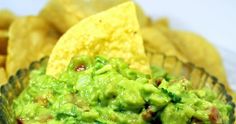 a glass bowl filled with guacamole and tortilla chips on the side