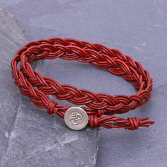 a red braided bracelet with a silver button on the clasp is sitting on a rock