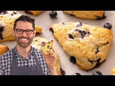 a man holding up a piece of blueberry scones in front of a group of scones