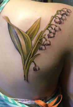 a woman's back with lily of the valley tattoo on her left side shoulder