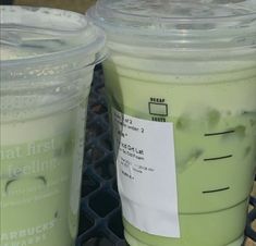 two plastic cups filled with green liquid sitting on top of a metal table next to each other