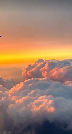 an airplane is flying high above the clouds at sunset or dawn in the sky with orange and yellow colors