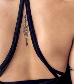 the back of a woman's black top with an arrow tattoo on her lower back