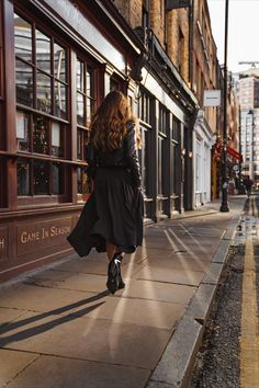 the woman is walking down the sidewalk in front of the storefronts with her back to the camera