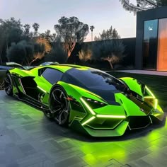 a green sports car is parked in front of a modern house at night with its lights on