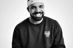 a black and white photo of a man with a beard wearing a beanie smiling at the camera