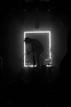 a man standing in front of a microphone on top of a stage under a neon light