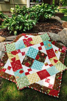 a patchwork quilt is laying on the ground in front of some rocks and plants