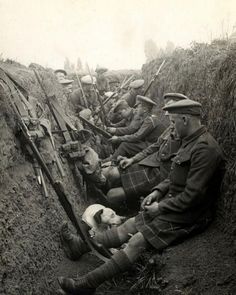 an old black and white photo of men in uniforms sitting on the side of a hill