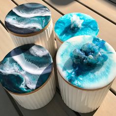 four different colored cupcakes with blue and white icing on them sitting on a wooden table