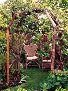 an outdoor garden with chairs and flowers on the arbor, surrounded by trees and shrubs