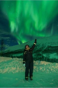 a man standing in the snow with his arms up and an aurora light behind him