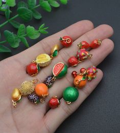 a person's hand holding seven different fruits and vegetables charms