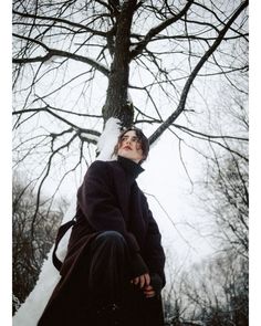 a woman sitting on top of a snow covered ground next to a tree with no leaves