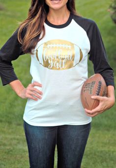 a woman holding a football in her hand and wearing a white shirt with gold foil on it