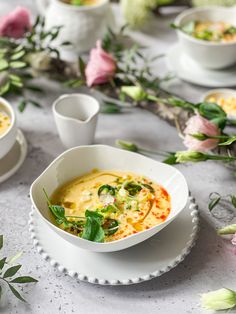 there is a bowl of soup on the table with other bowls and flowers around it