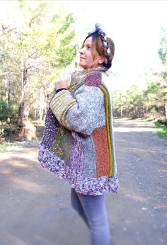 a woman walking down a dirt road holding onto a colorful jacket on her shoulders and looking off into the distance