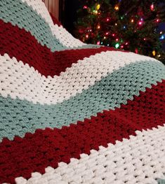 a crocheted blanket sitting on top of a couch next to a christmas tree