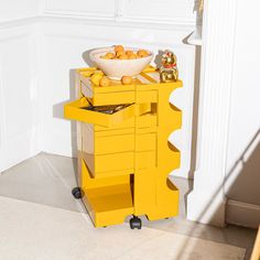 a bowl of oranges sits on top of a yellow cart in the corner of a room