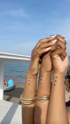 two women with matching tattoos on their arms near the ocean and beach, one holding her hand up to her head