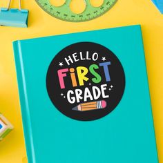 a blue notebook with the words hello first grade on it next to a ruler and other school supplies