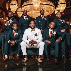 a group of men in tuxedos posing for a photo together with chandeliers behind them