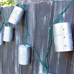 four tin can lights are hanging on a wooden fence with green string attached to them