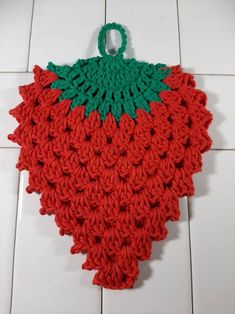 a crocheted strawberry with green leaves on it's back, sitting on a tile floor