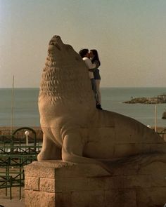 a man and woman standing next to a statue of a lion on top of a beach